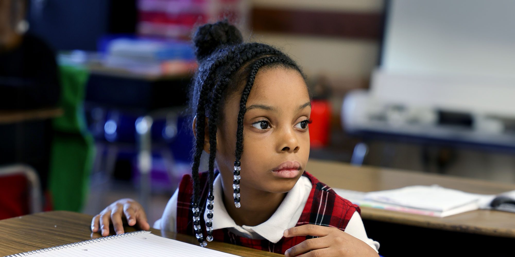 Young student with beaded braids listening attentively at her desk.